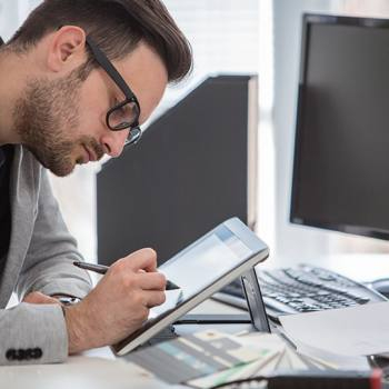 Designer using digital tablet at desk, modern office workflow with print and document tools